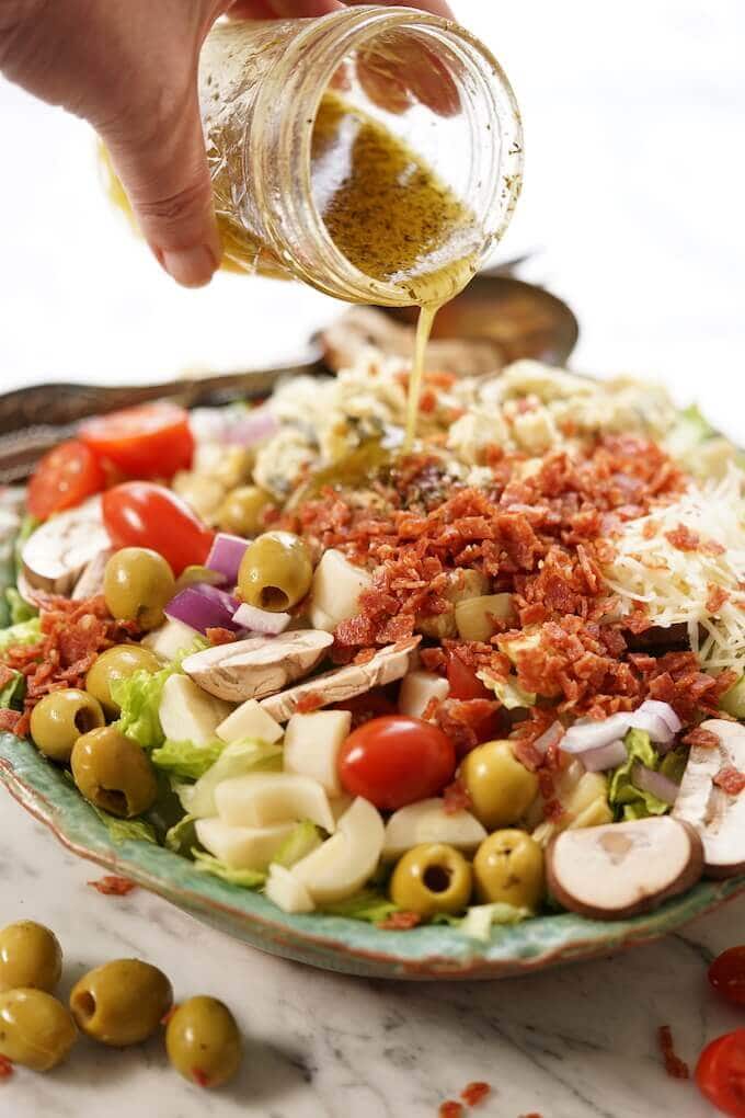 A green salad in a bowl with a jar of salad vinaigrette being added to the salad.