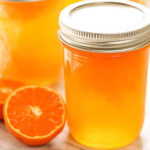 Orange Jelly in jar with sliced mandarin on the side.