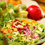 Shaved Brussel Sprout Salad in green bowl topped with pomegranate arils and sliced peaches