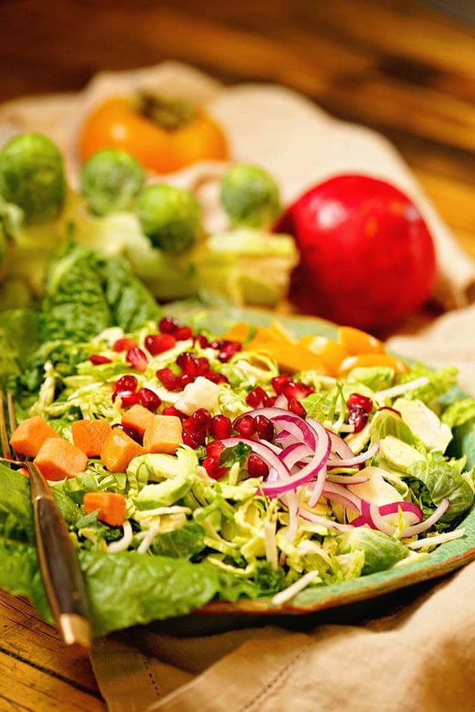 Shaved Brussel Sprout Salad in green bowl topped with pomegranate arils and sliced peaches.