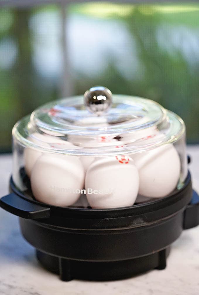 Egg Cooker filled with eggs on white marble counter.