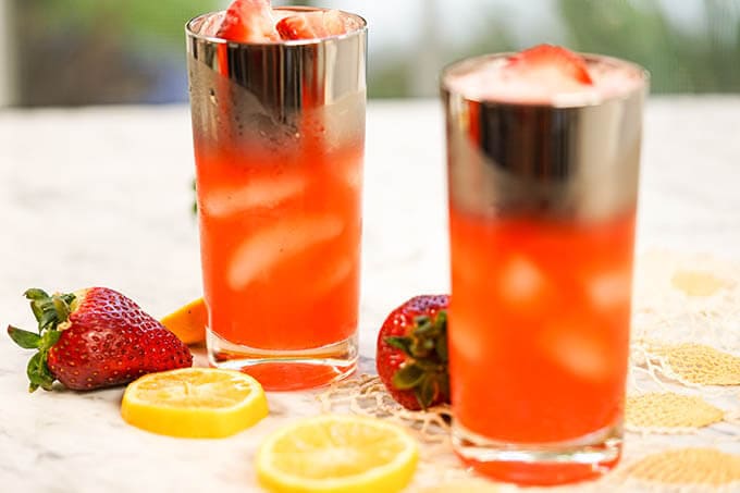 Two glasses filled with strawberry lemonade, garnished with lemons and strawberries!