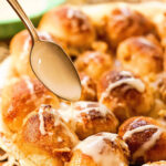 Monkey bread in baking dish with glaze being spooned over the rolls.
