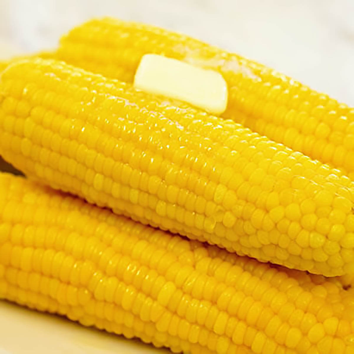 A platter of cooked corn on the cob with a bit of melting butter on top.