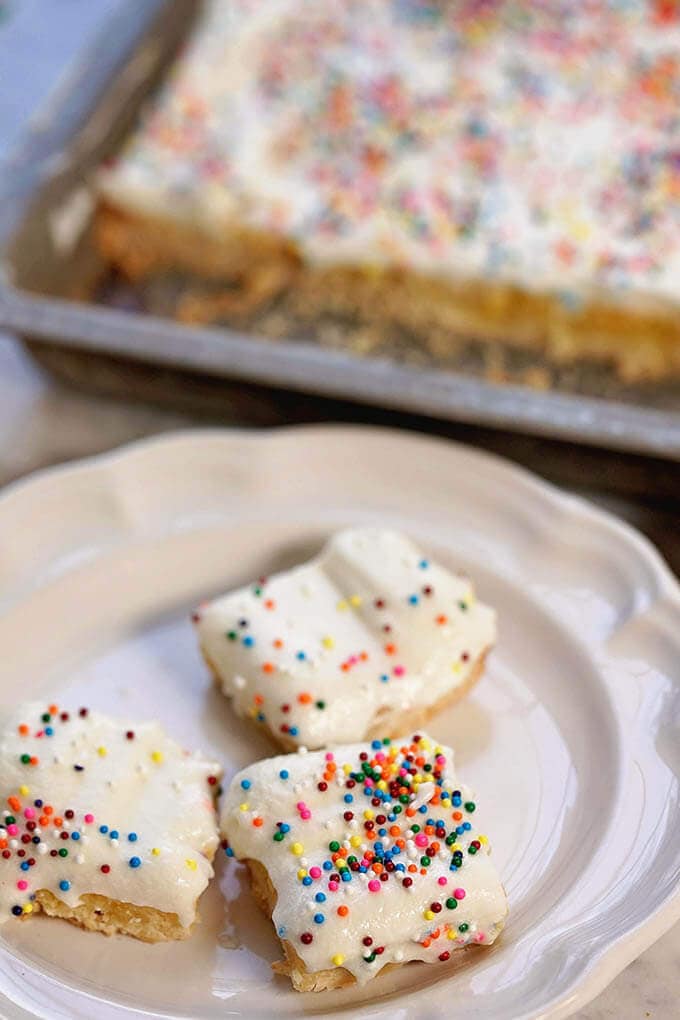 Easy Lemon Bar Recipe with several bars on white plate with a pan of bars ready to eat!