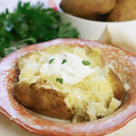 Baked potato in bowl, topped with butter and sour cream.