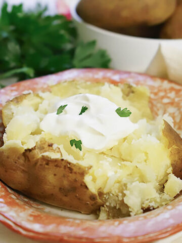 Baked potato in bowl, topped with butter and sour cream.