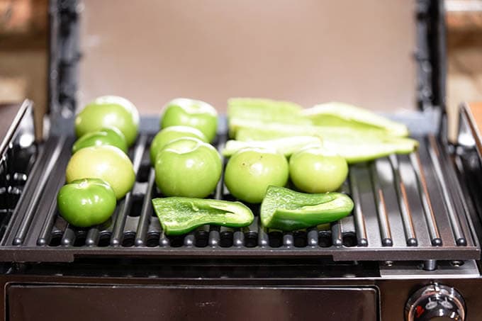 Tomatillos, peppers and jalapeños roasting on grill.