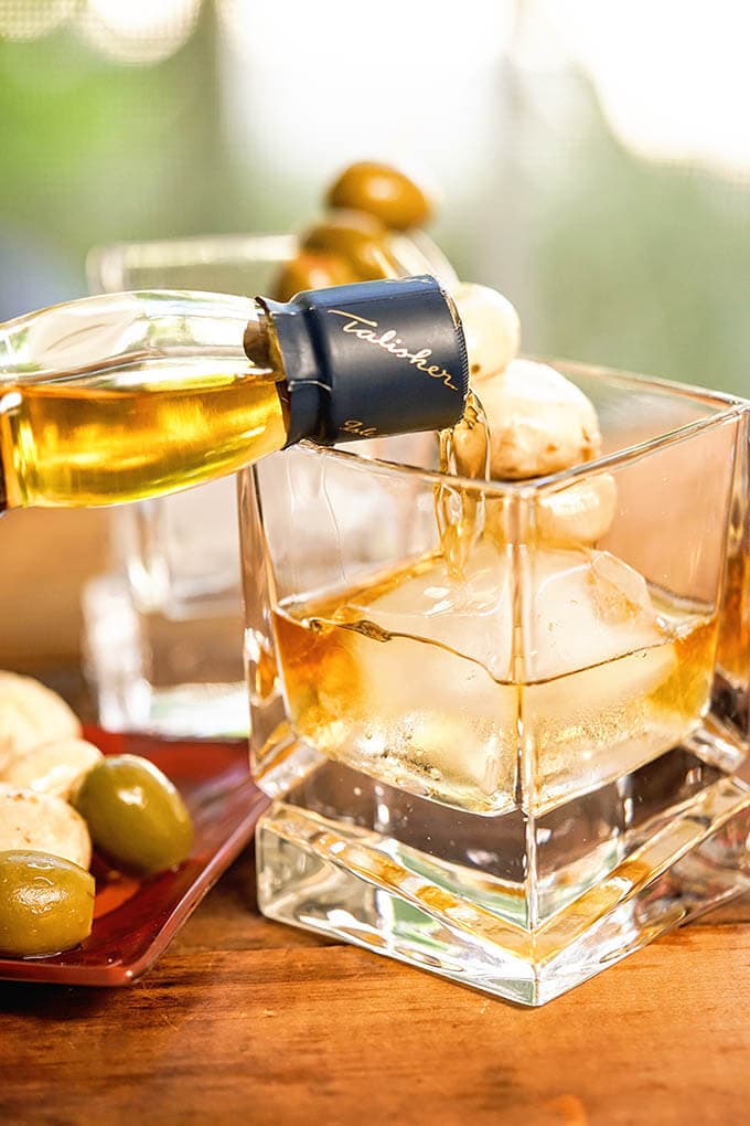 Whiskey pouring into a cocktail glass with an ice cube.