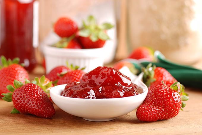 Strawberry Freezer Jam in white bowl surrounded by strawberries
