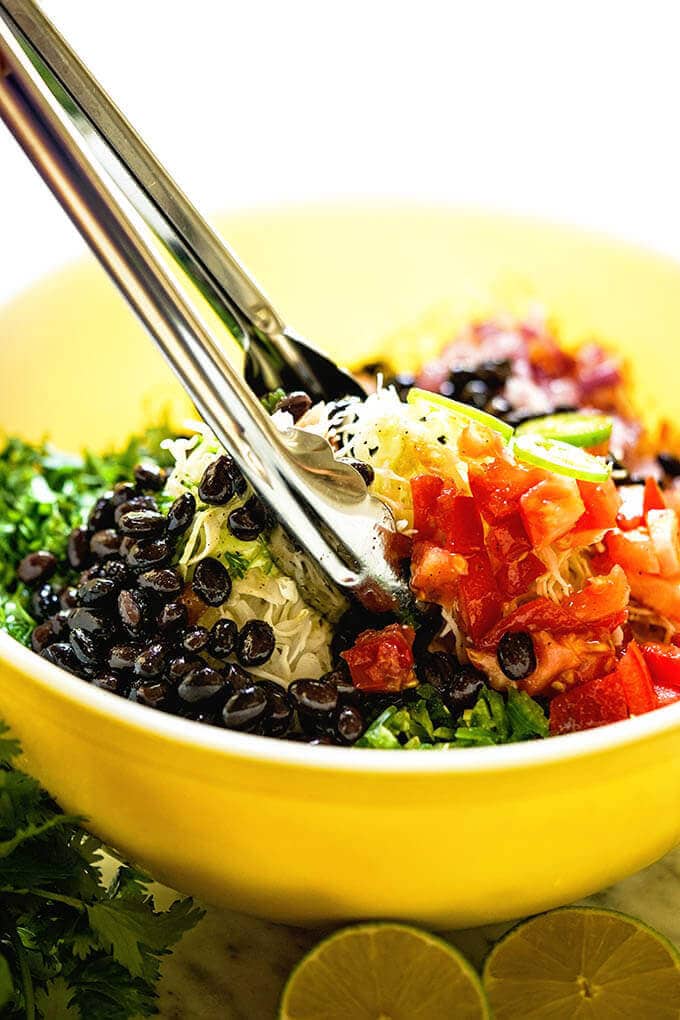 Mayo-free slaw in yellow bowl with silver tongs to toss the slaw.