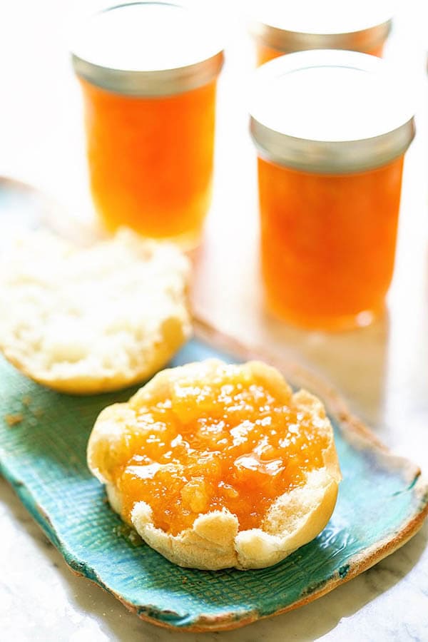 Apricot Pineapple Jam on English muffin, surrounded by jars of jam. 