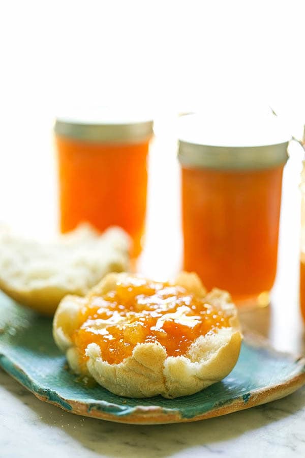 Apricot Pineapple Preserves spread on a roll on plate with jars of preserves.