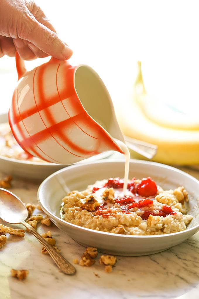 Oatmeal with strawberries in bowl. Milk is poured in from pitcher.