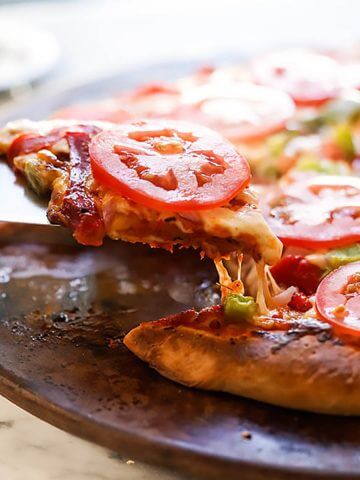 Sliced, baked thick crust pizza topped with tomatoes.