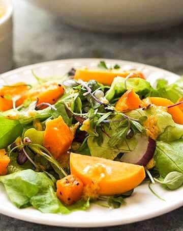 Fall Harvest salad with persimmons and roast squash on white plate with fork.