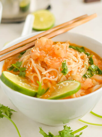 Thai red curry soup in white bowl topped with lime and served with chopsticks.