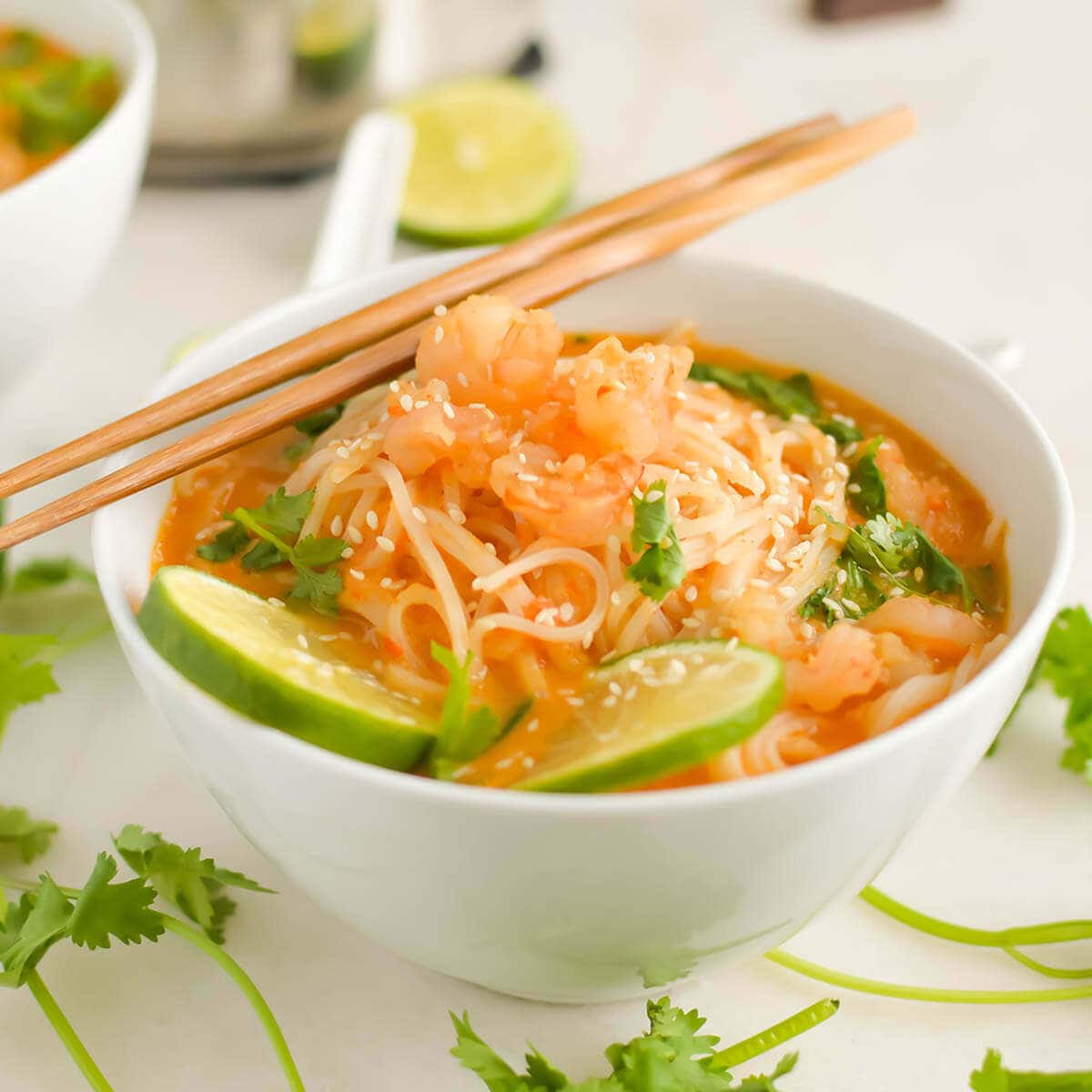 Thai red curry soup in white bowl topped with lime and served with chopsticks.
