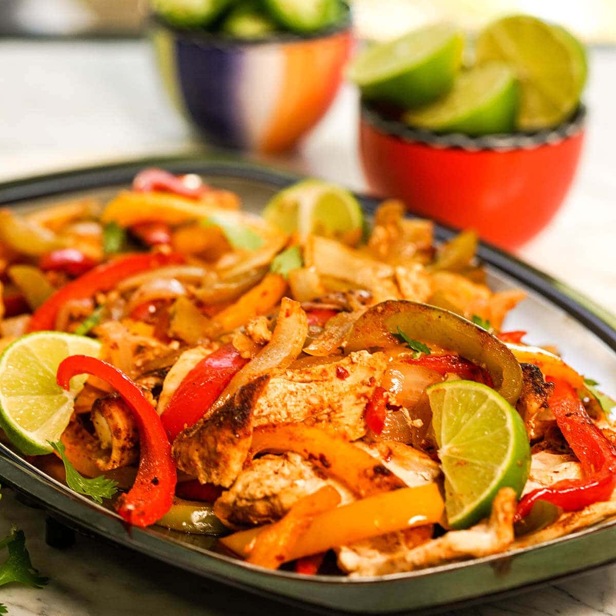 Fajitas on pan with bowls of lime and jalapeños on the side.