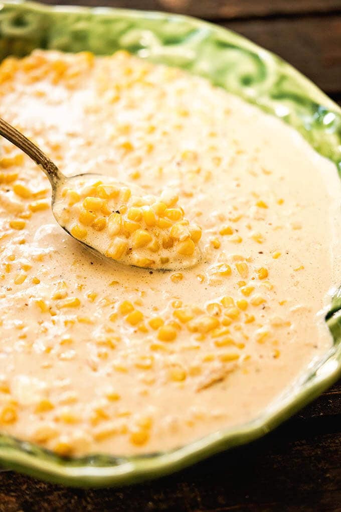 Creamed corn in green bowl with spoon.