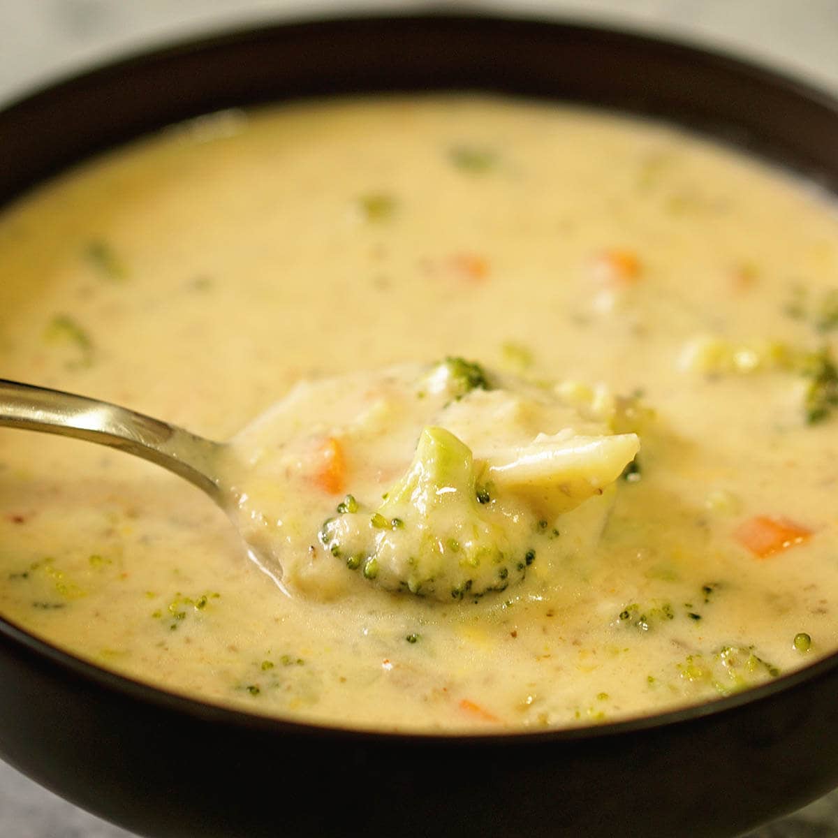 Cheesy soup in black bowl with spoon.