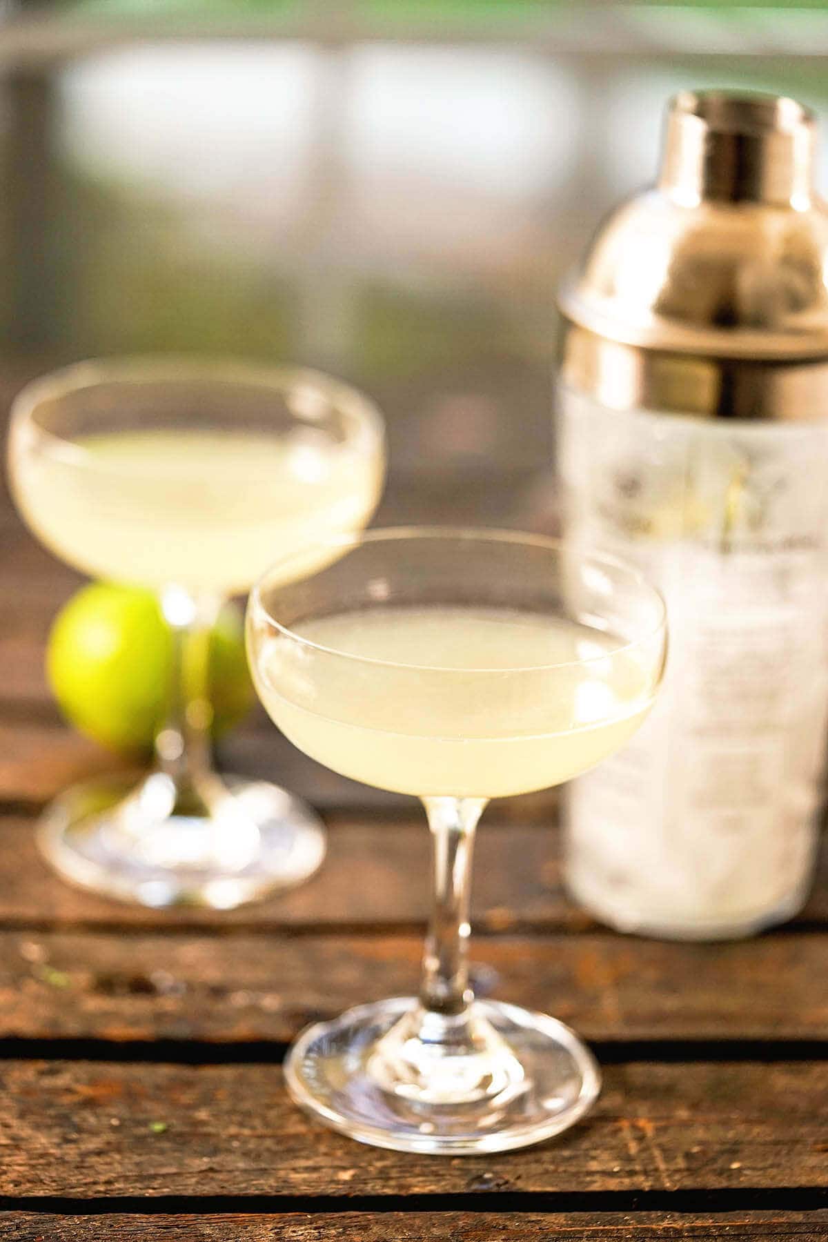 Cocktails with shaker on wooden board with lime.