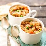 White bowl filled with stew on blue platter with spoons.