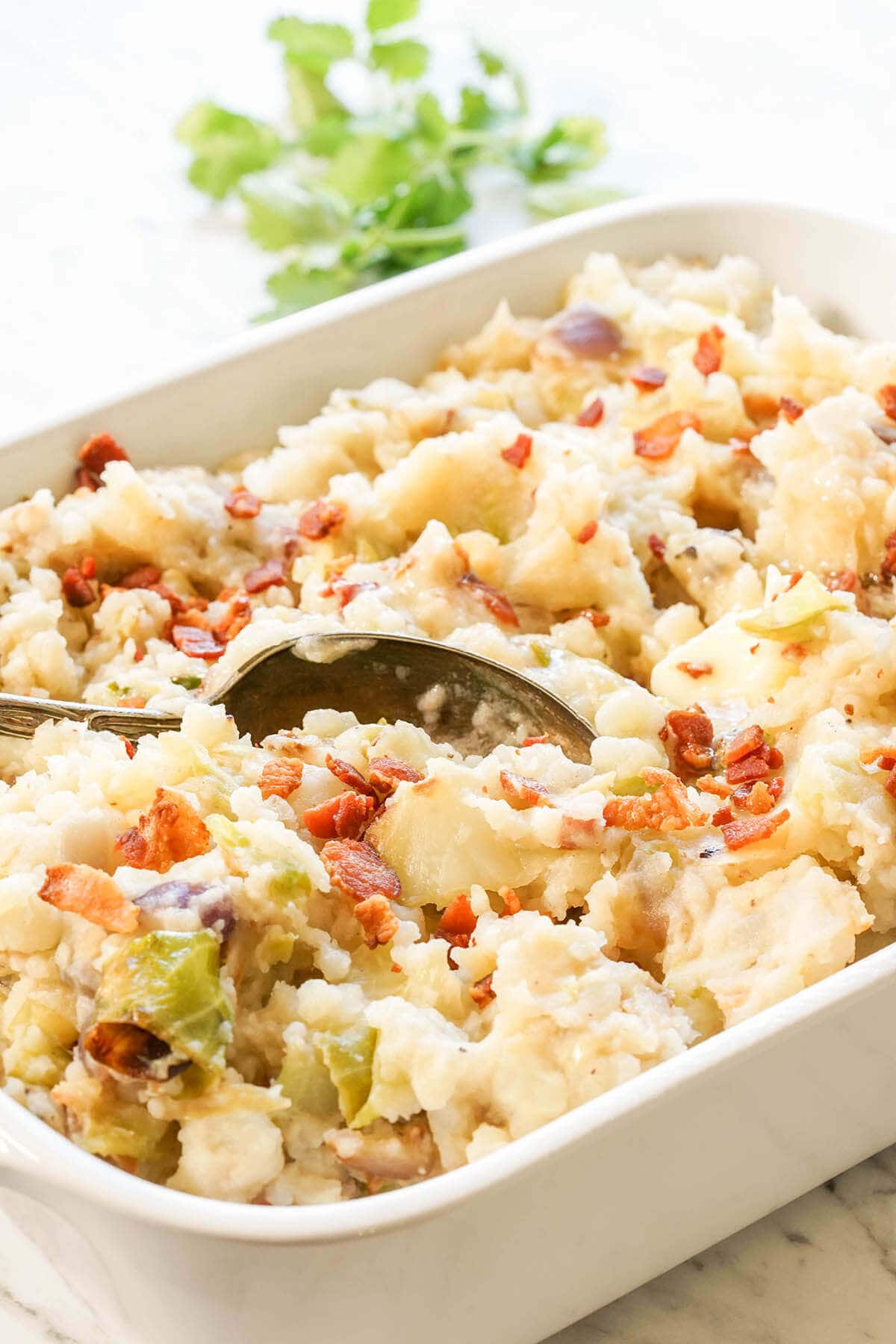 A Casserole dish filled with Colcannon Potatoes served with spoon.