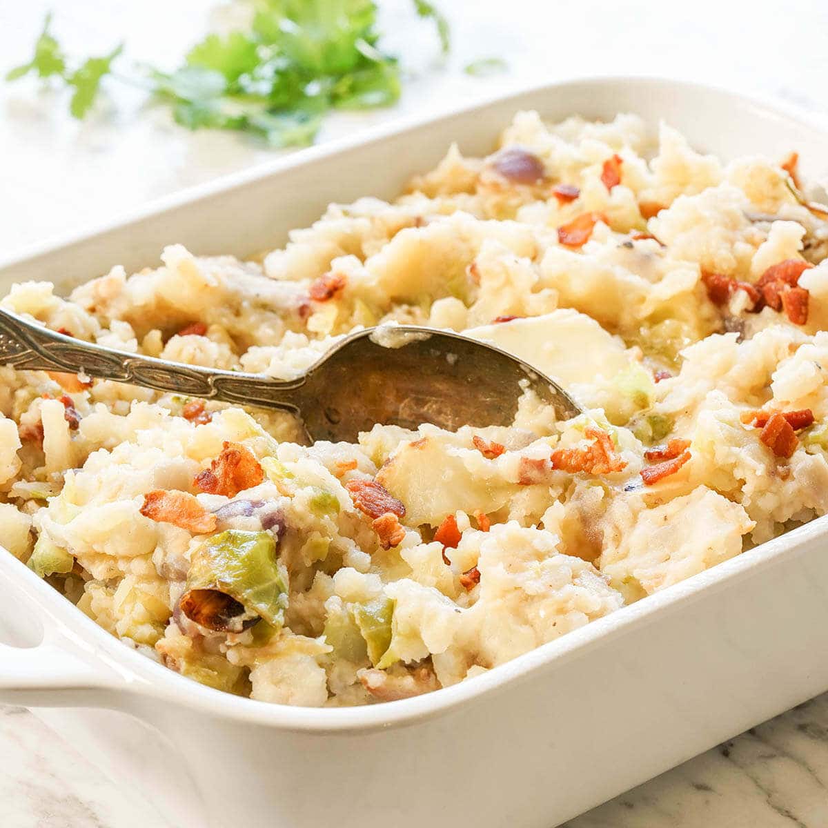 Colcannon in white dish topped with crispy bacon with spoon