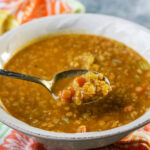 Golden lentil soup in white bowl with spoon scooping out a serving.