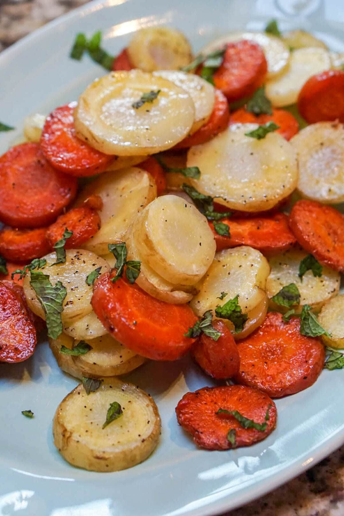 A plate filled with pretty sliced roasted carrots, topped with mint. 