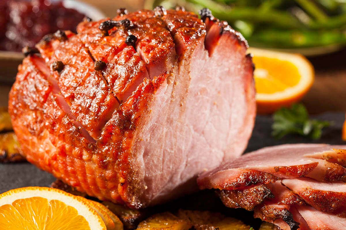 Sliced holiday ham on platter with oranges