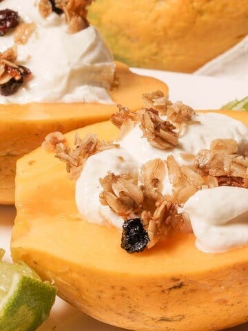 Golden papaya breakfast bowl topped with thick greek yogurt, crunchy granola surround by wedges of lime.