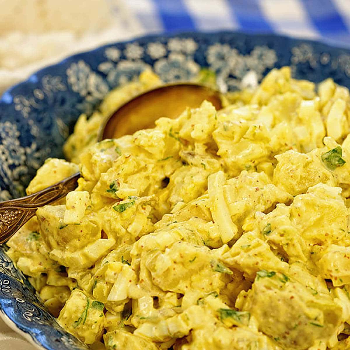 A blue bowl on a white and blue tablecloth filled with deviled egg potato salad.