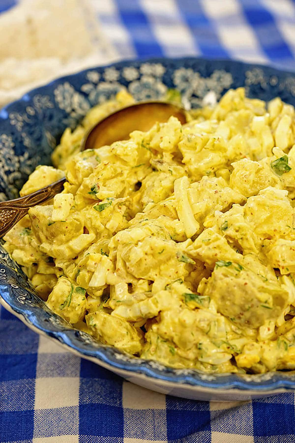 Creamy potato salad in a blue bowl with a serving spoon.