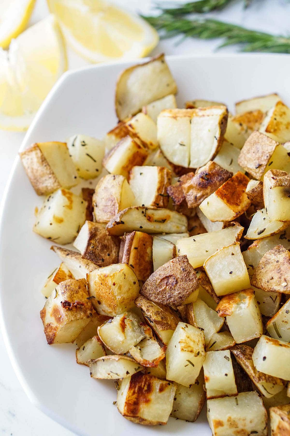 Roasted potatoes on white plate with lemon and rosemary.
