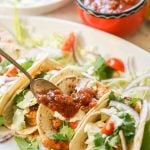 Tacos on white platter topped with pico de Gallo.