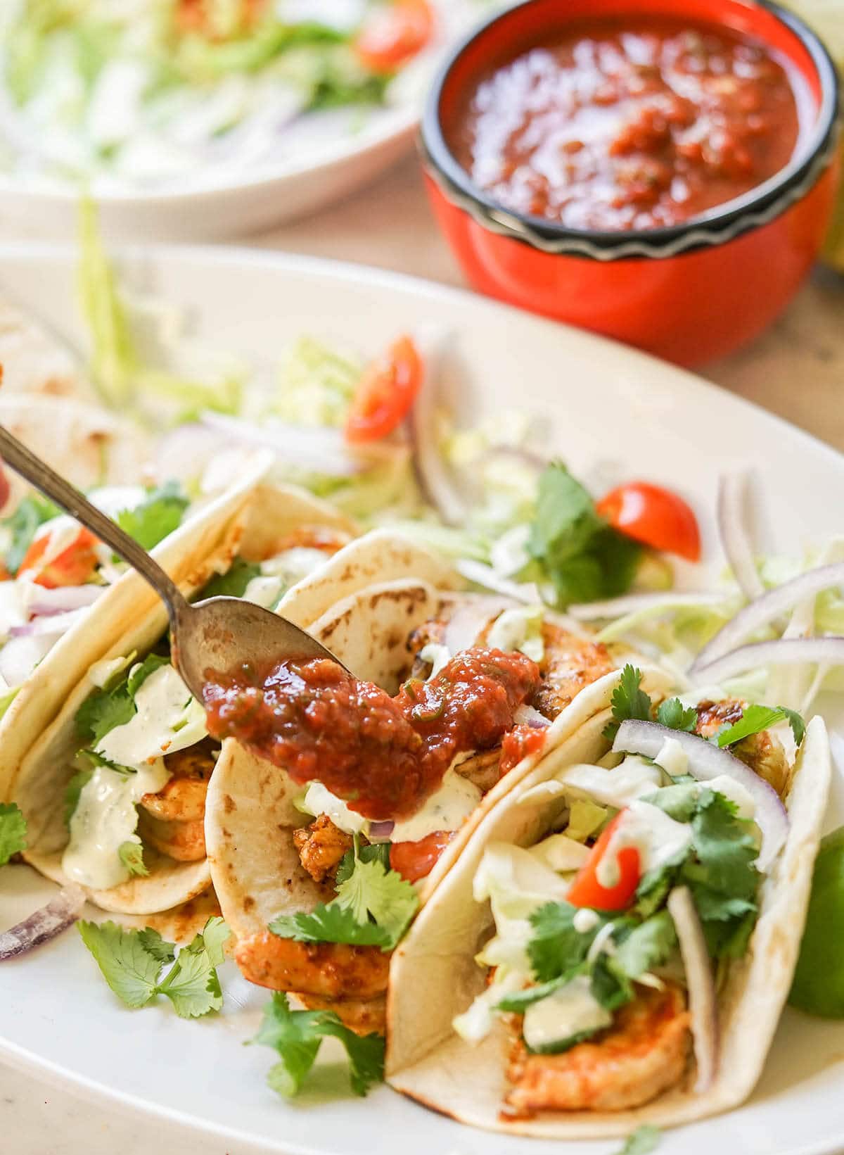 Tacos on white platter topped with pico de Gallo.