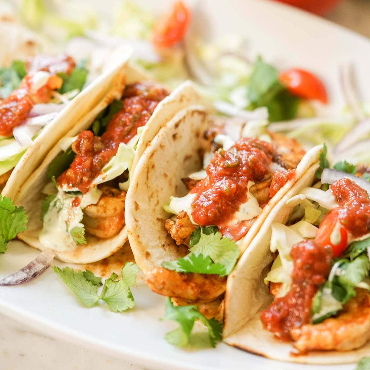 Shrimp tacos topped with cabbage, tomatoes and cilantro on white platter