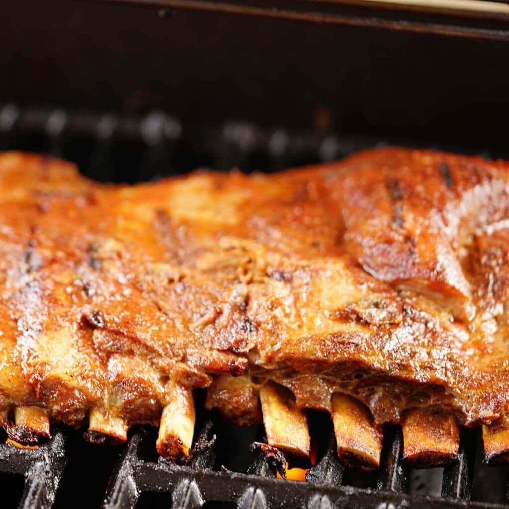 A slab of grilled ribs slathered with bbq sauce on grill.