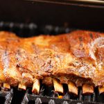 A slab of grilled ribs slathered with bbq sauce on grill.