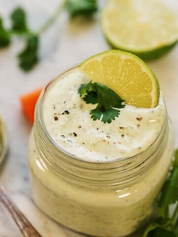 Cilantro Garlic Sauce in glass jar topped with sliced lime and a sprig of cilantro