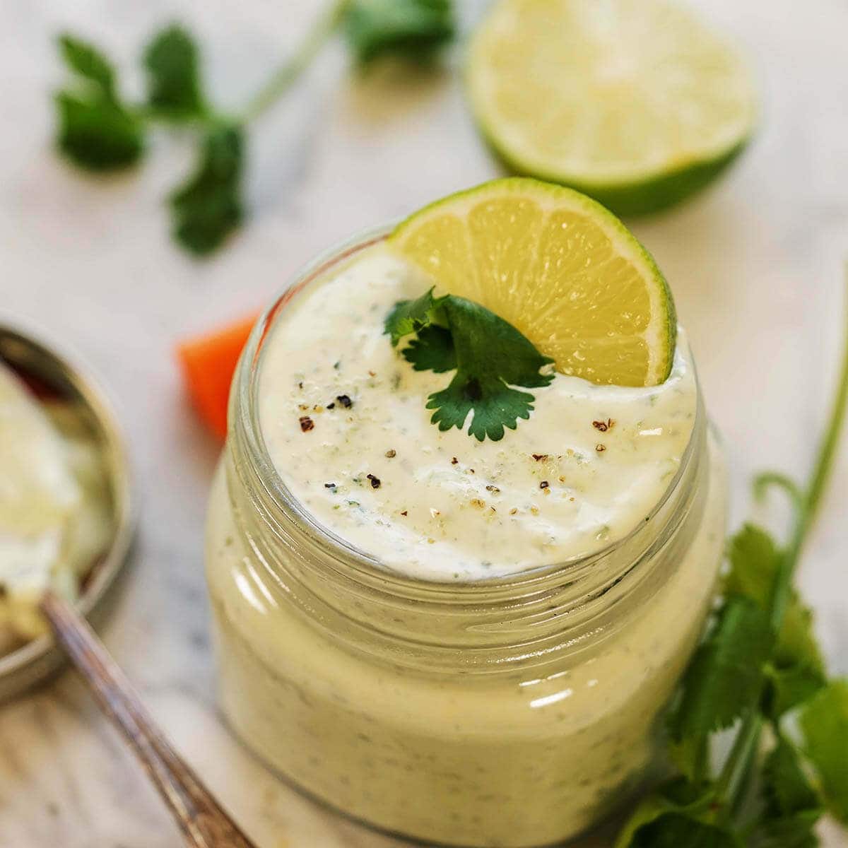 Cilantro Garlic Sauce in glass jar topped with sliced lime and a sprig of cilantro 