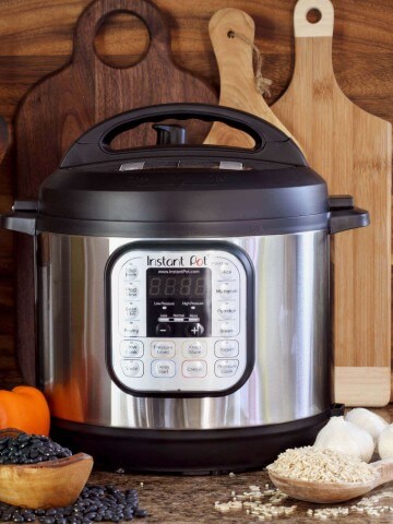 Instant pot sitting on granite counter top alongside beans, garlic and wooden spoon.