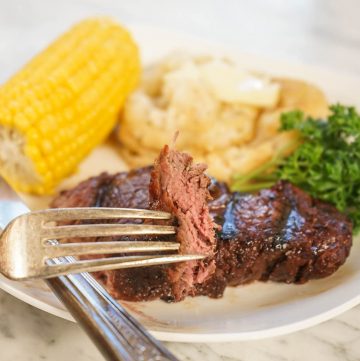 Tenderloin steak on plate with potatoes and corn.