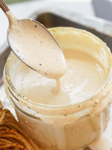 White BBQ Sauce in jar with spoon drizzling sauce back into the jar.