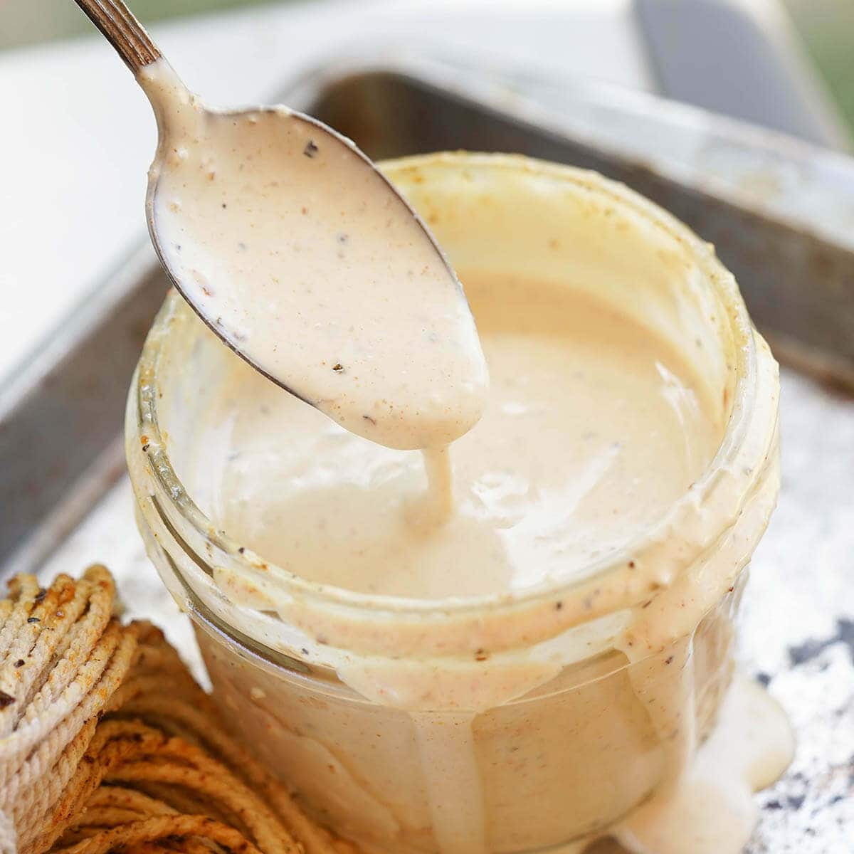 White BBQ Sauce in jar with spoon drizzling sauce back into the jar. 