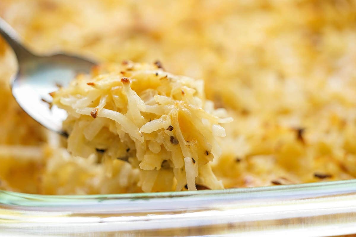 Casserole filled with Cracker Barrel Cheesy Potatoes being dished up with spoon.