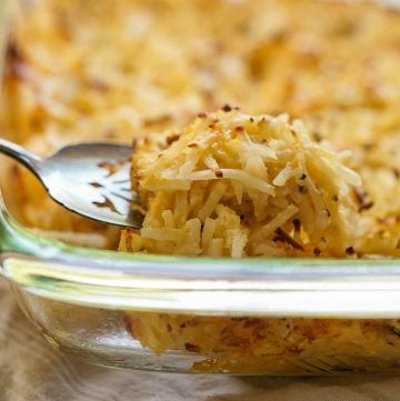 Casserole dish filled with Cracker Barrel Cheesy Potatoes being serve with a spoon.