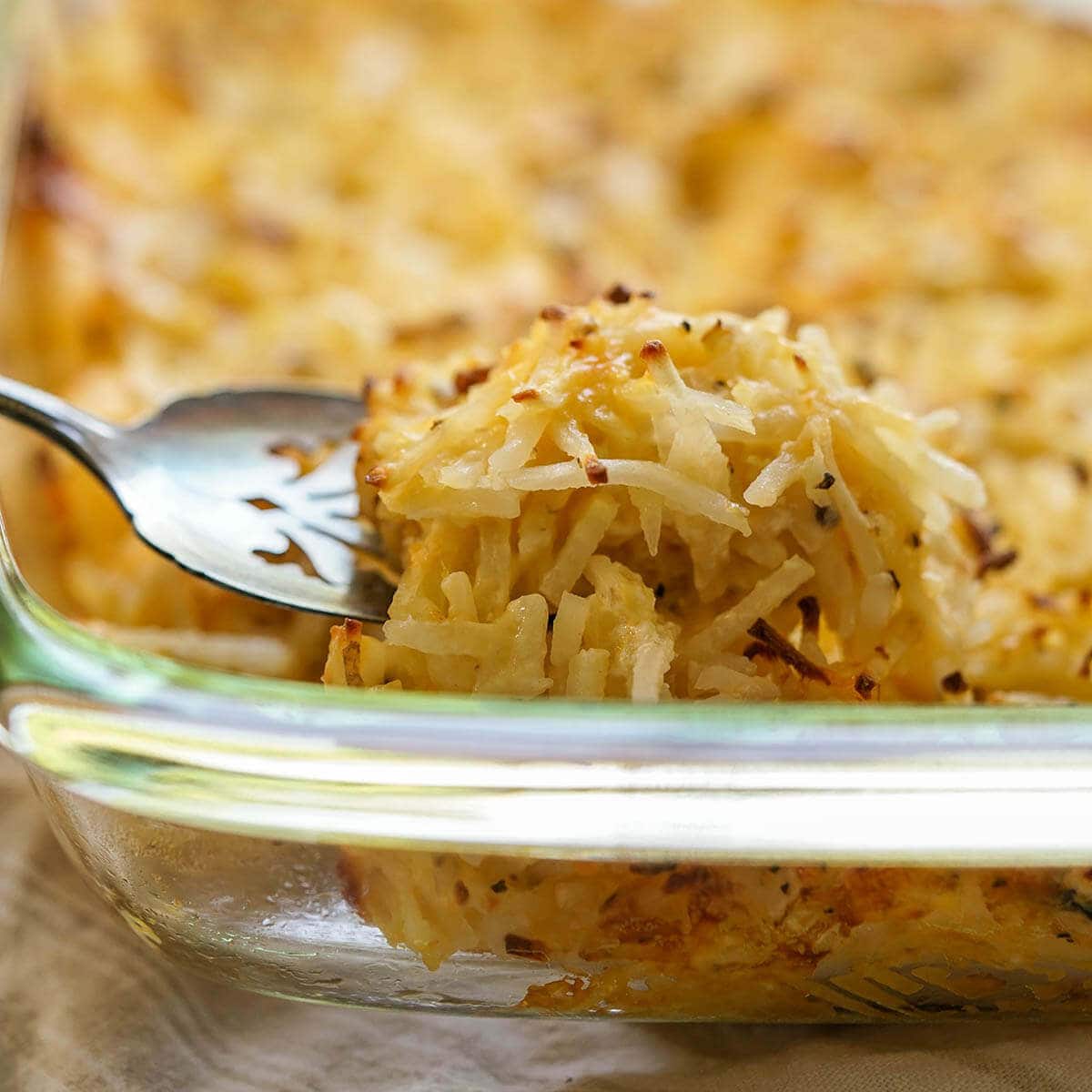 Casserole dish filled with Cracker Barrel Cheesy Potatoes being serve with a spoon.